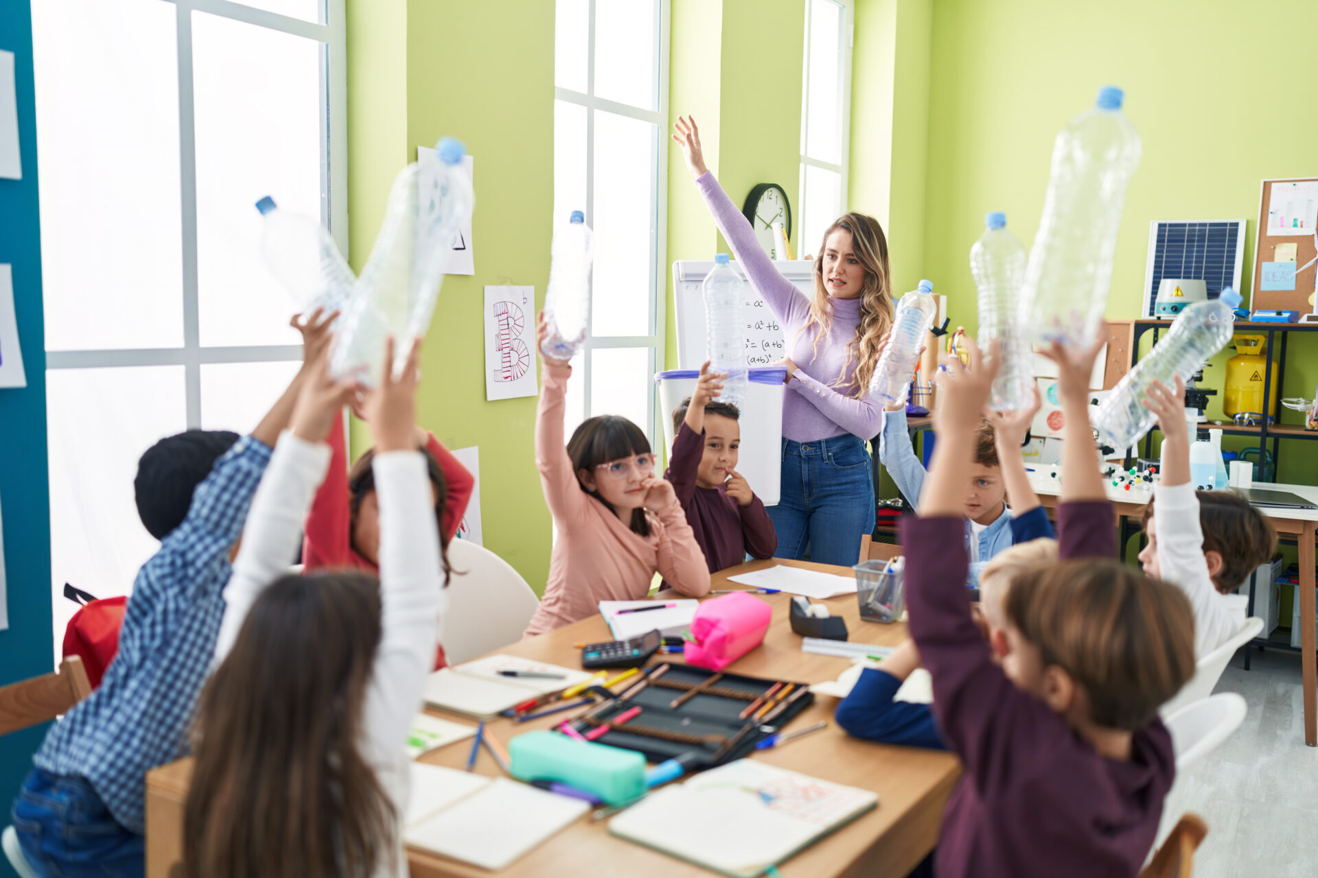 Woman and group of kids having recycling lesson holding empty bottle at classroom