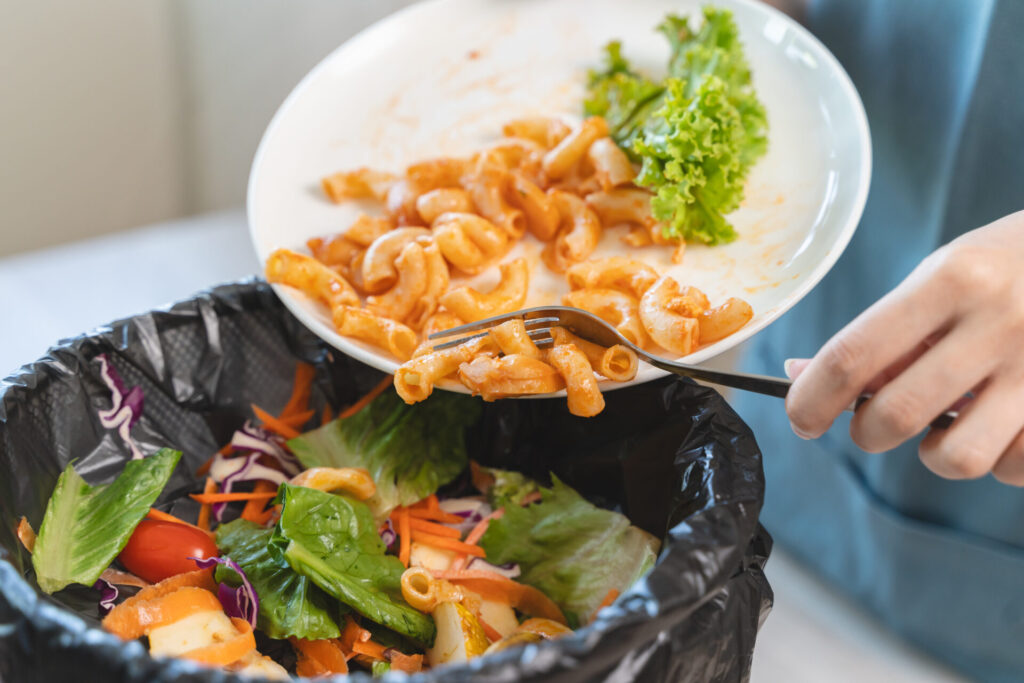 Compost from leftover food in the meal in household, female hand holding left over meal use fork scraping waste, rotten vegetable throwing away into garbage, trash or bin. environmentally responsible